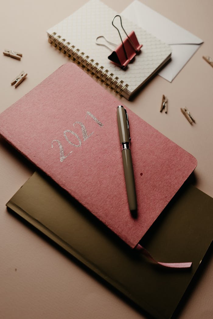 A stylish still life of a 2021 planner, notebooks, and pen with soft moody lighting.