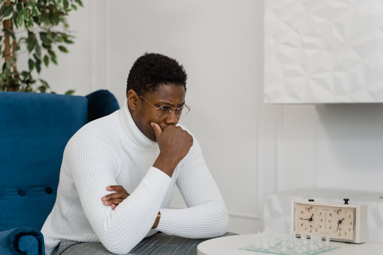 Thoughtful man in white sweater playing chess indoors, emphasizing strategy and focus.