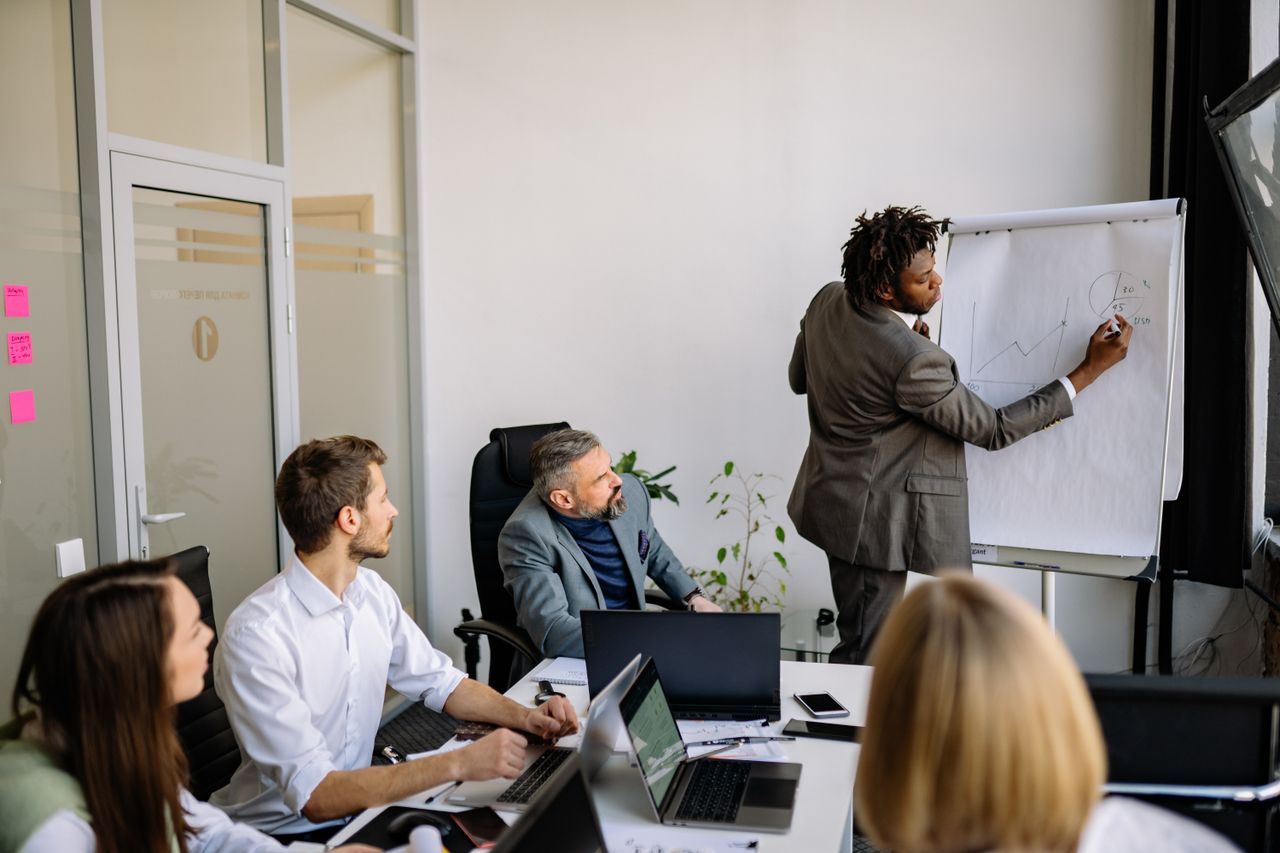 A diverse team in a modern office engaged in a strategic business meeting led by a presenter.